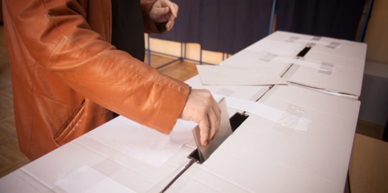 A person drops their ballot into a voting box.