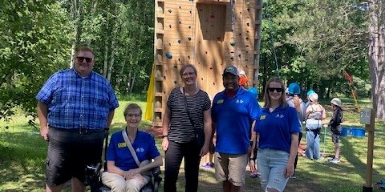 A group of people stand in front of the accessible climbing tower at CNIB Lake Joe. From left to right: MPP Graydon Smith, Monique Pilkington, Executive Director, CNIB Lake Joe, Moreen Miller, an Ontario Trillium Foundation (OTF) volunteer, Eugene Chong, CNIB Lake Joe General Manager, and Emilee Schevers, CNIB Lake Joe Staff.