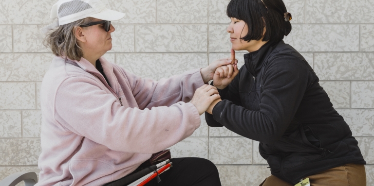 an intervenor uses tactile sign language to communicate with a client.