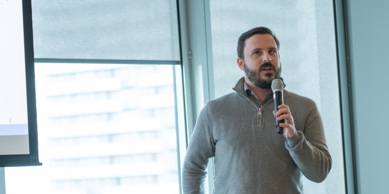 A man in a grey sweater speaking into a microphone 