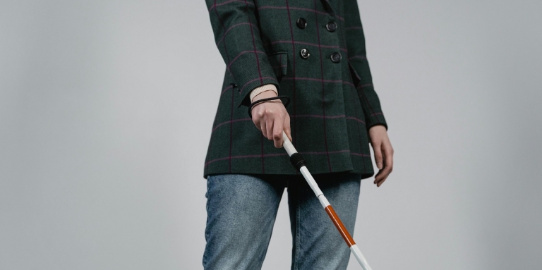 A person with a white cane poses for a photo in an office corridor. 