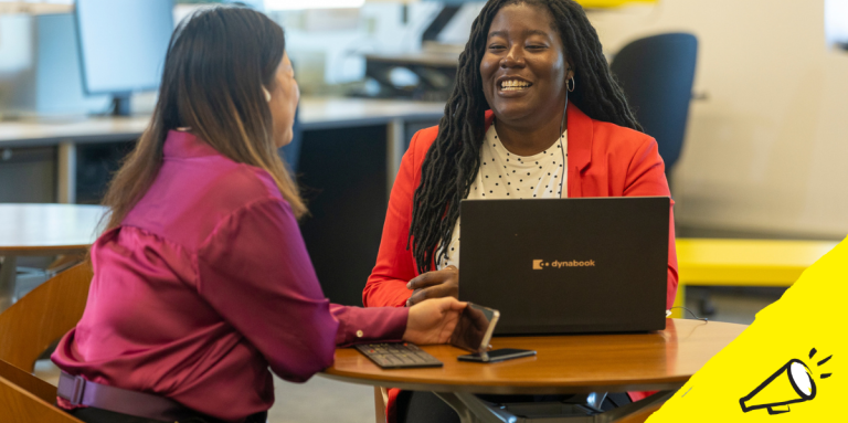 Two women work together in the office using their phone and laptop. A black and white illustration of a megaphone appears against a yellow background.