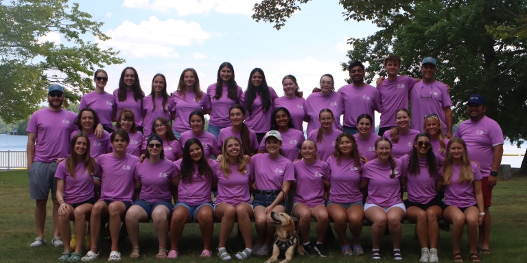 The 2026 seasonal staff team is posing on the lawn. There are 34 people wearing shorts and pink tshirts.