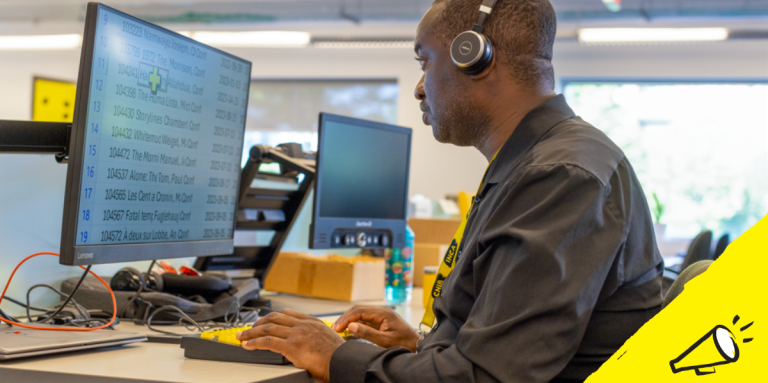 A man sits at a desk while using screen magnification technology on a desktop computer, as well as a high contrast keyboard