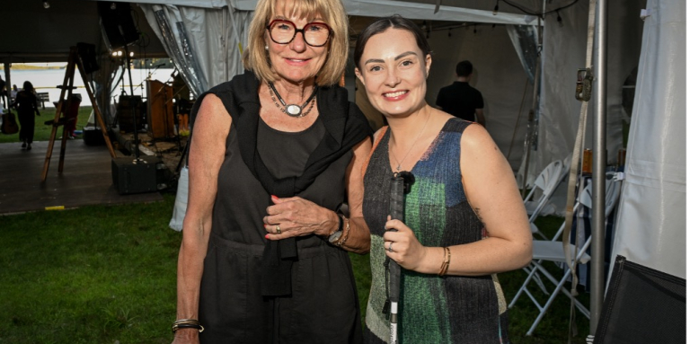 CNIB board member, Jane Savidant (left) and Molly Burke (right) and smile for a posed photo in front of a tent at the Lake Joe Live event.