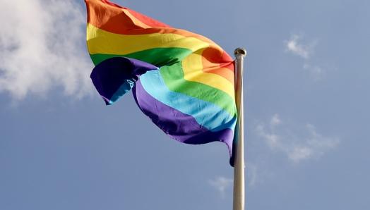 A colourful Pride flag waves in the wind on a flag post. 