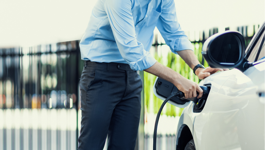 At a public charging station, a man holds an electric vehicle charger plug and charges his car.