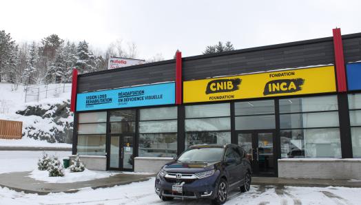 Exterior of CNIB Sudbury Hub featuring bright VLRO and CNIB Foundation signage. A gentle snowfall covers the exterior parking lot