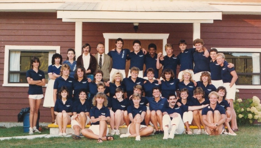 Photo de l'équipe du personnel de 1986 (35 hommes et femmes vêtus de chemises de golf bleues et de shorts blancs) posant à l'extérieur du bâtiment du personnel pour le 25e anniversaire du camp Lake Joe d'INCA. 