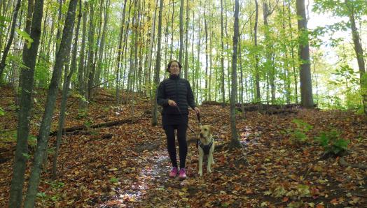 Marie-Claire and Rhonda, walking through a lush, green forest – the ground covered with colourful autumn leaves.