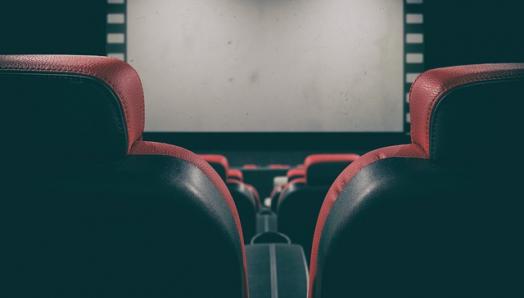 Une salle de cinéma vide. Des rangées de chaises sont empilées devant un écran sombre. 