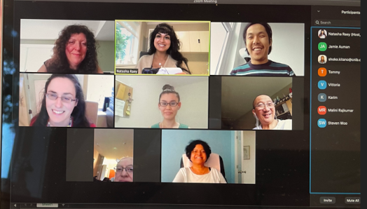 A Zoom call with eight participants is displayed on a laptop screen.