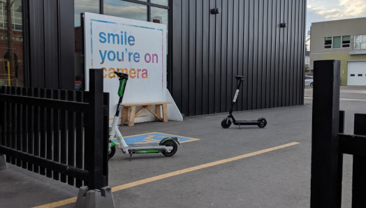 Two e-scooters sit side-by-side on a sidewalk outside a business in Edmonton.]