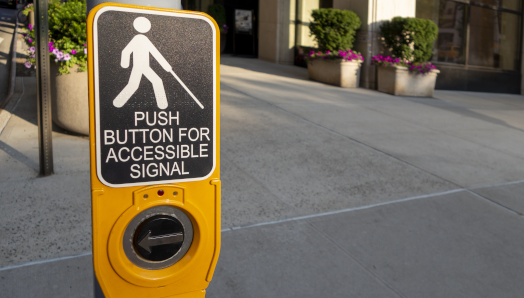 Un bouton-poussoir jaune/noir de signal d'accessibilité pour piétons sur un poteau.