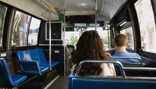 The interior of a city bus. The view is from the rear of the bus, looking towards the front. A few passengers are seated.