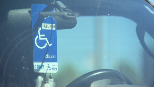 An Alberta accessible parking permit is hung on a car's rear-view mirror. The photo is taken from outside the vehicle, looking through the windshield.