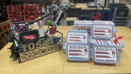 A robot sits beside a stack of braille blocks on a table.