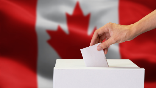 A person casting their ballot in a ballot box. A Canadian flag in the background.