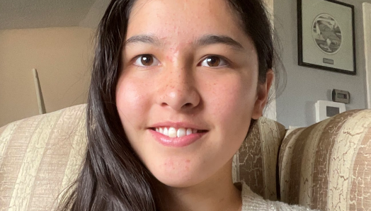 A headshot of Anna Kim smiling while sitting on a couch.