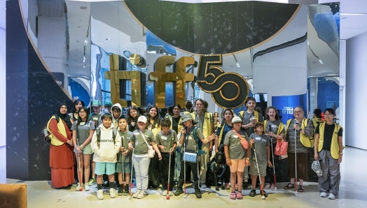 In the lobby of the TIFF Lightbox, a large group of young campers and CNIB volunteers pose for a group photo in front of a giant “TIFF 50” sign.