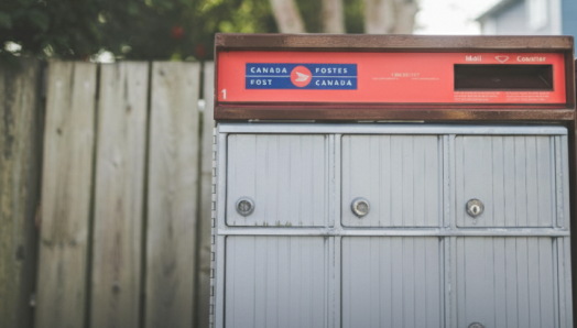 Canada Post mailbox with a wooden fence behind it.