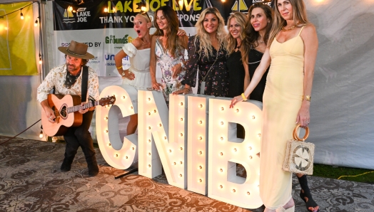 Six women wearing semi formal attire stand on a stage behind large lights in the shape of the letters C-N-I-B.