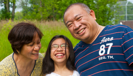 A mother, father, and teenage daughter laugh together; the daughter is wearing glasses.