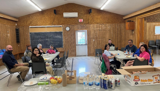 Participants gathered at an informational session about the Legal Support Program. Approximately 10 participants sit around two tables in a community meeting space, accompanied by a table with refreshments.