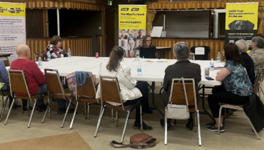 Nine community members sit around a table having a conversation. 