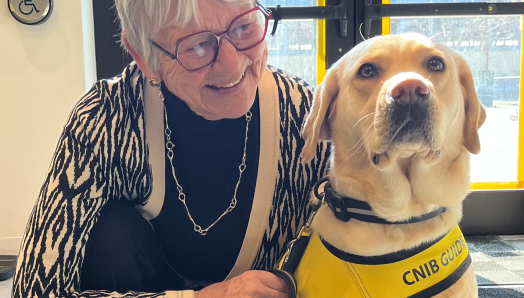 Jane crouching down beside a CNIB guide dog. She is looking at the dog and smiling.